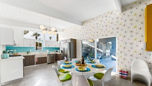 A modern kitchen with white cabinets, a turquoise countertop, and a dining area with white chairs and a round table set for six.