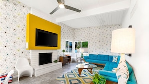 A living room with a TV mounted on a yellow wall, a fireplace, a blue sofa, and a patterned rug.