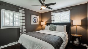 Quarto com cama, duas luminárias de cabeceira, ventilador de teto e janela com persianas.