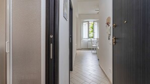 A hallway with a dark wooden door, a white wall, and a window with white curtains. - Marina View Terrace by Wonderful Italy (Rapallo)