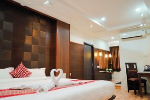 Een hotelkamer met een groot bed, een houten hoofdbord, een bureau met een stoel, en een airconditioning op de muur.