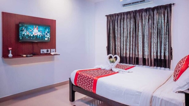 A hotel room with a bed, a TV mounted on the wall, a ceiling fan, and a window with curtains. - RD HOTEL (Perundurai)