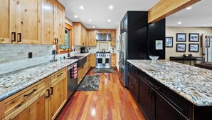 Une cuisine moderne avec des meubles en bois, des plans de travail en granit, une cuisinière en acier inoxydable et un réfrigérateur noir.