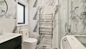 A bathroom with a marble wall, a toilet, a sink, a glass shower enclosure, and a bathtub.