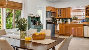 A modern kitchen with wooden cabinets, a dining table with chairs, a potted plant, and a bowl of fruit.