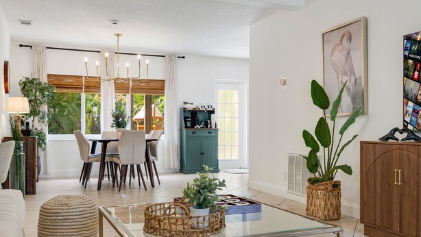 A spacious living area with a glass coffee table, a dining table with chairs, a sofa, a cabinet, and a large window with curtains.