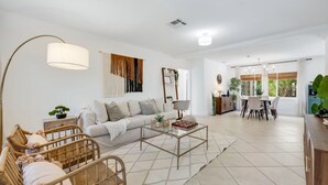A living room with a sofa, coffee table, and chairs, a dining area with a table and chairs, and a kitchen area with cabinets and a counter.