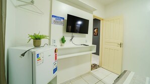 A compact hotel room with a white refrigerator, a flat-screen TV mounted on the wall, a small potted plant, and a door leading to another room. - Flat Pet Friendly pr x ao Aeroporto (Fortaleza)
