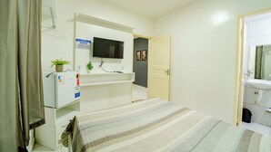 A hotel room with a bed, a TV mounted on the wall, a small desk with a plant, and a door leading to a bathroom. - Flat Pet Friendly pr x ao Aeroporto (Fortaleza)
