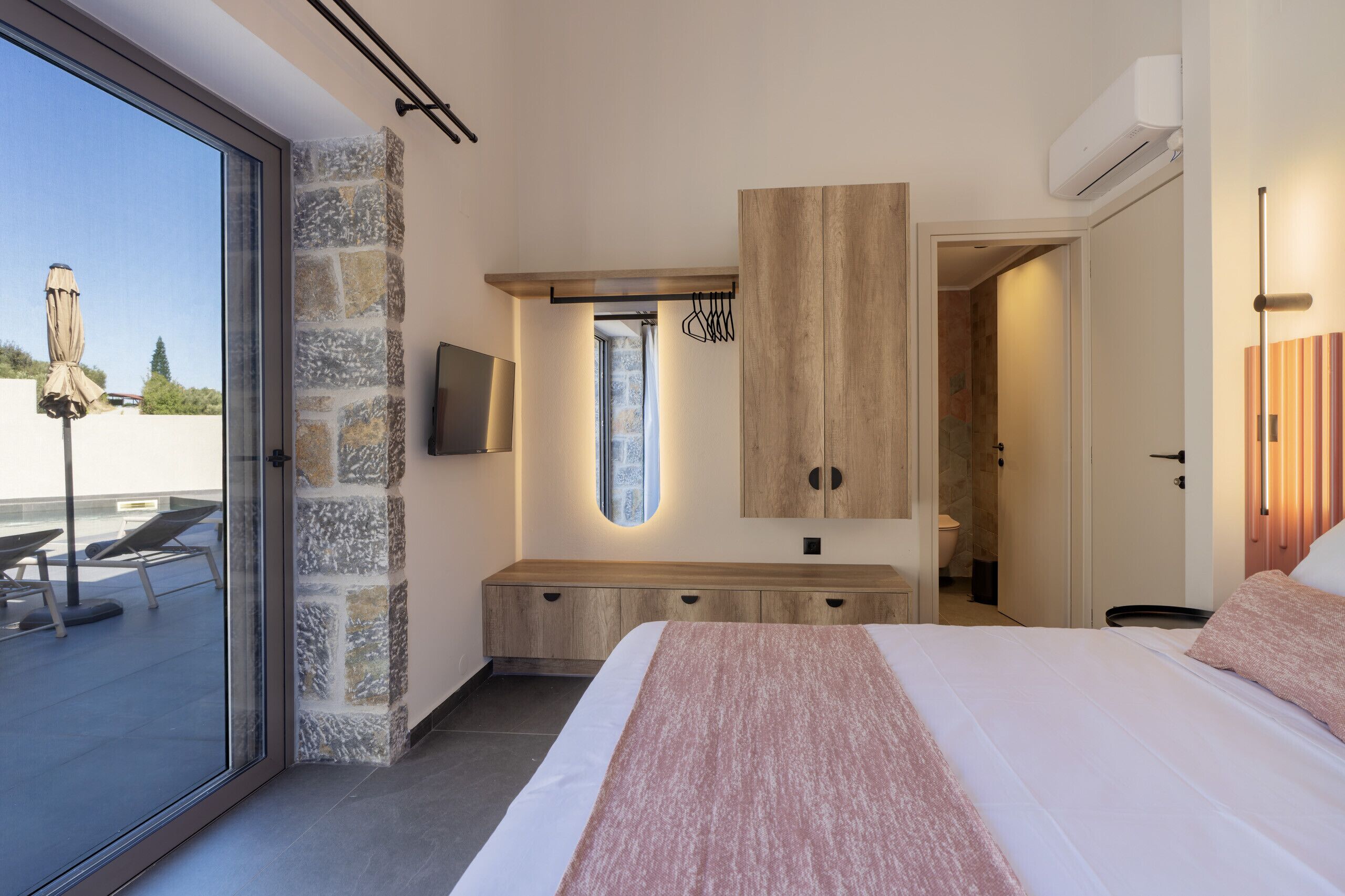 Ein Schlafzimmer mit einem großen Bett, einer Steinsäule, einer hölzernen Bank und einem an der Wand befestigten Fernseher.