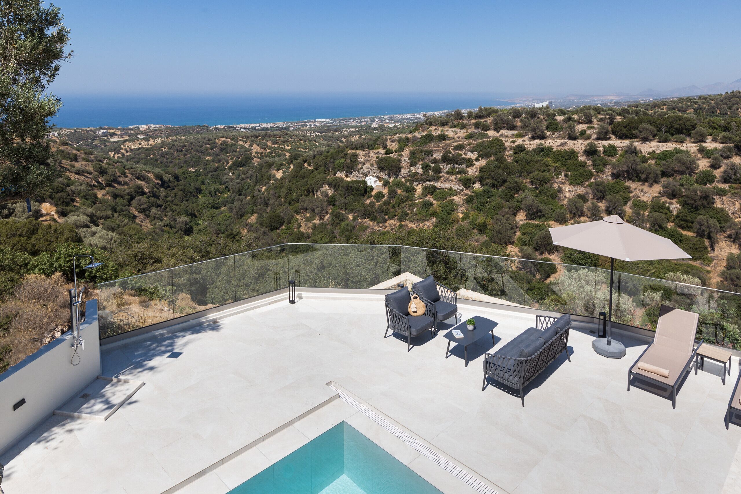 A rooftop pool area with lounge chairs and an umbrella, overlooking a coastal landscape.
