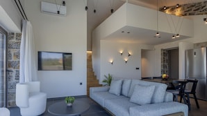 A modern living room with a grey sofa, a round coffee table, and a staircase leading to a kitchen area. - Villa Ioannis - With Private Heated Pool (Rethymno)