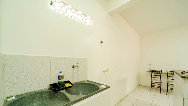A small kitchen with a granite countertop, a sink, and a faucet. There is a bottle of dish soap and a sponge on the counter. The kitchen has white cabinets and a tiled backsplash. - Flat Para 2 Pessoas a Poucos Metros do Aeroporto (Fortaleza)