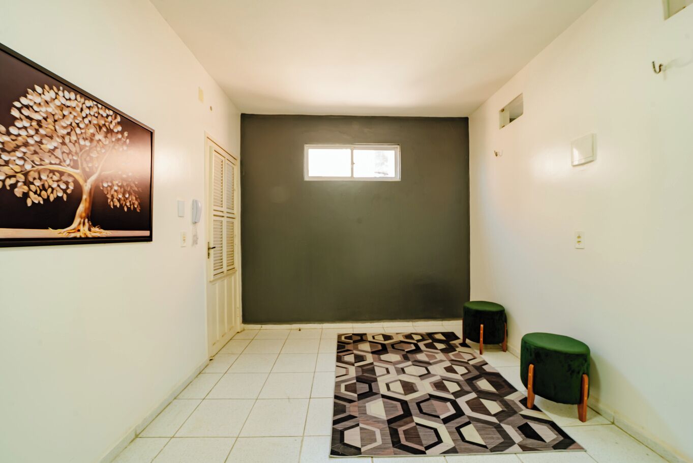A hallway with a patterned rug, a green stool, and a door with shutters.