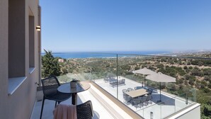 A balcony with a glass railing, outdoor furniture, and a view of the sea and landscape. - Villa Santa Irini 1 - With Heated Pool (Rethymno)