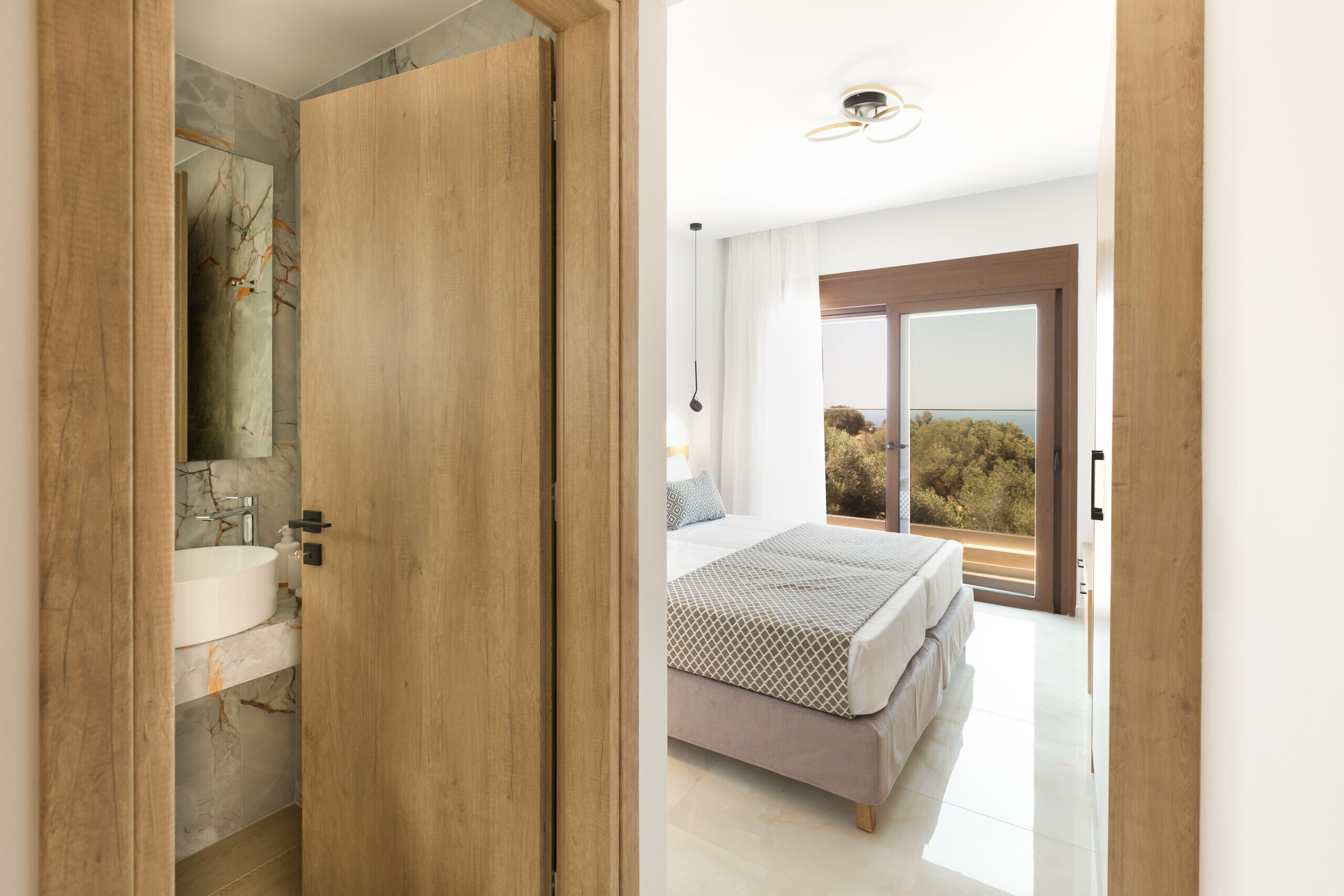 A bedroom with a bed, a bathroom with a sink, and a view of the outdoors.