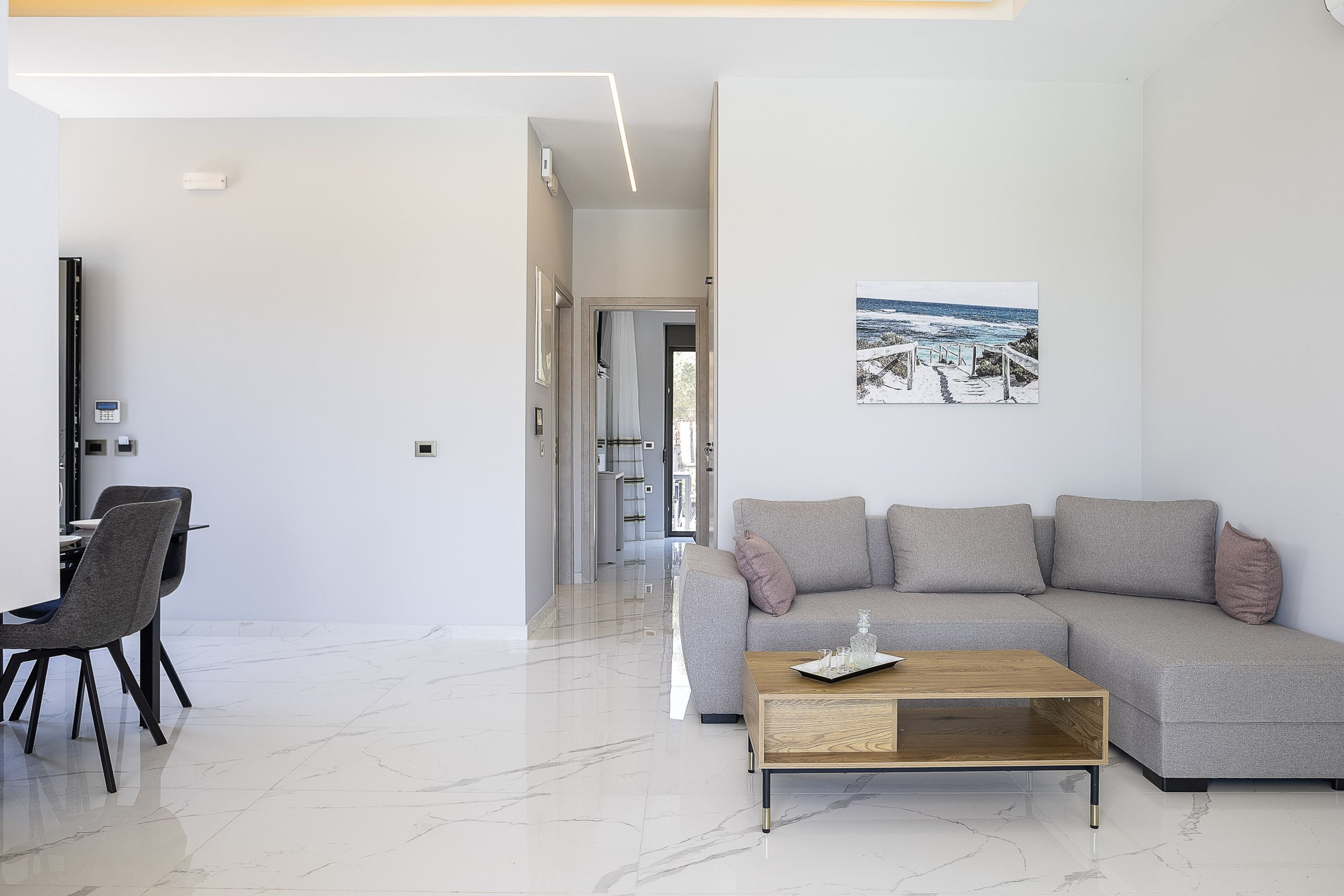 Een moderne woonkamer met een grijze bank, een houten salontafel en een eethoek met stoelen.