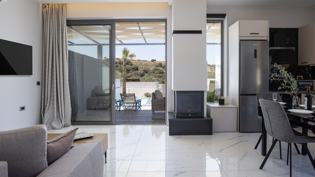 A modern kitchen with a built-in stove, a dining area with a table and chairs, and a large sliding glass door leading to an outdoor patio. - Villa Me - With Private Pool (Mylopotamos)
