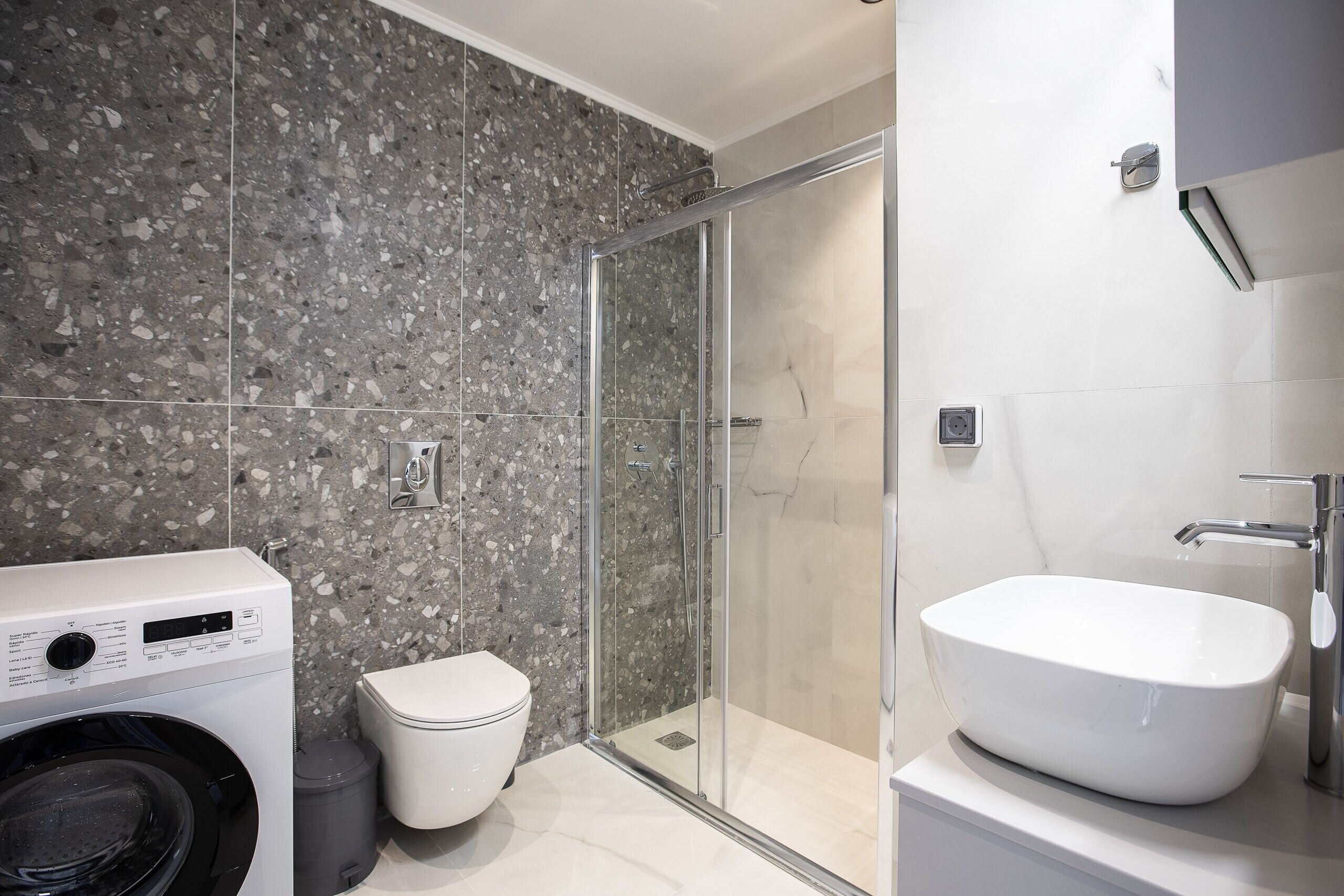 A modern bathroom with a glass-enclosed shower, a standalone sink, and a washing machine.
