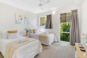 A hotel room with two beds, a ceiling fan, a window with curtains, and artwork on the wall.