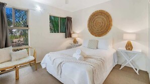 Une chambre à coucher comprenant un lit, une chaise, une table de chevet, une lampe, un ventilateur de plafond et une fenêtre avec des rideaux.