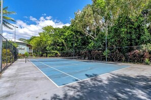 Ein Tennisplatz im Freien mit Netz, umgeben von Bäumen und einem Gebäude im Hintergrund.