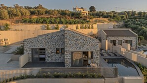 A stone building with a pool and outdoor seating, surrounded by greenery and a hillside in the background.