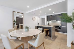 A modern kitchen with a central island, a dining area with a round table, and a large mirror on the wall.