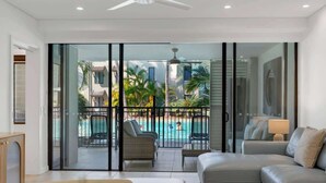 Ein modernes Wohnzimmer mit einer Couch, einem Couchtisch und Blick auf einen Swimmingpool durch große Glasfenster.