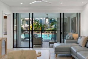 Un soggiorno moderno con un divano, un tavolino da caffè e vista su una piscina attraverso ampie vetrate.