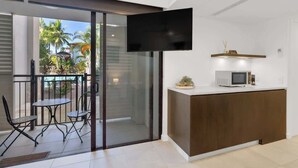 Un intérieur moderne avec une porte-fenêtre coulissante donnant sur un balcon, un téléviseur à écran plat fixé au mur et un petit coin cuisine équipé d’un four à micro-ondes.