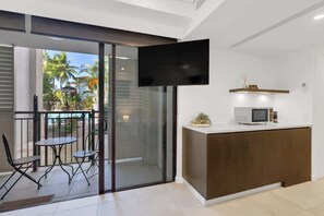 A modern interior with a sliding glass door leading to a balcony, a flat-screen TV mounted on the wall, and a small kitchen area with a microwave.