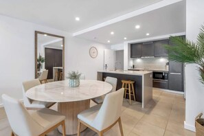 A modern kitchen with a central island, a dining area with a round table, and a large mirror on the wall.