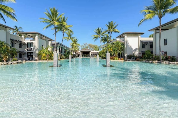 A resort with a clear pool, palm trees, and modern buildings.