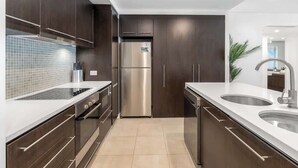 Une cuisine moderne avec des meubles en bois foncé, des appareils électroménagers en acier inoxydable et un plan de travail blanc.