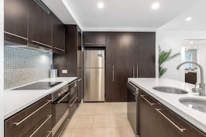Une cuisine moderne avec des meubles en bois foncé, des appareils électroménagers en acier inoxydable et un plan de travail blanc.