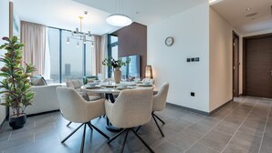 A modern dining area with a round table, four chairs, and a potted plant. - Skyline Views 2BR, Steps from a Park, Minutes Drive to Meydan Golf Club (Dubai)