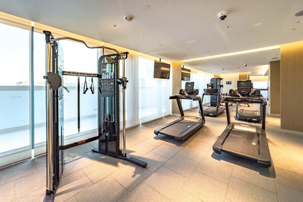 Une salle de sport équipée de tapis de course, d’une machine de musculation et de grandes fenêtres.
