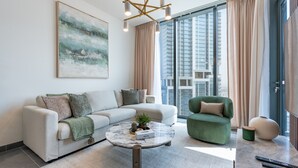 A modern living room with a sofa, armchair, and coffee table, large windows with curtains, and a city view. - Skyline Views 2BR, Steps from a Park, Minutes Drive to Meydan Golf Club (Dubai)