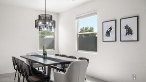 Un comedor moderno con una mesa larga, seis sillas, una lámpara colgante negra y dos cuadros enmarcados con estampados de animales en la pared.