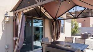 Un patio exterior con una parrilla, una mesa de comedor, sillas y una zona cubierta con luces.