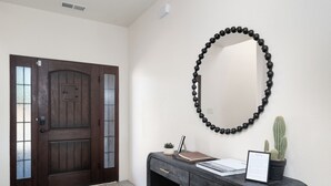 Una recepción con una puerta de madera oscura, un collar de cuentas negras, un cactus en maceta y un letrero de bienvenida enmarcado.