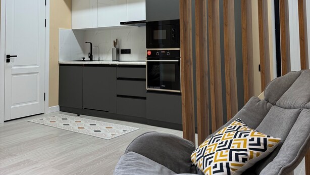 A modern kitchen with grey cabinets, a black oven, and a yellow pendant light. - Serenity   (Dushanbe)