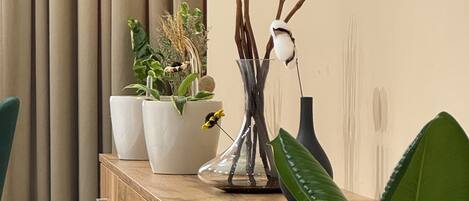A wooden desk with three potted plants, a vase with sticks, and a lamp.