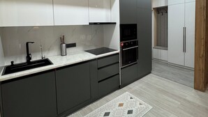 A modern kitchen with dark cabinetry, a white countertop, and a patterned rug. - Serenity   (Dushanbe)