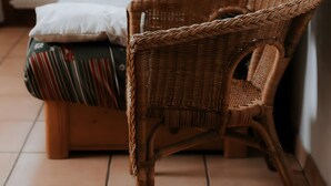 Une chaise en osier placée à côté d’un lit avec une literie à rayures et un oreiller.