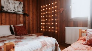 Une pièce aux murs lambrés, avec deux lits, un luminaire fixé au mur et une fenêtre.