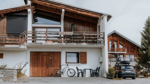 Un bâtiment à deux étages doté d’un balcon en bois, avec un vélo et une voiture garés devant.