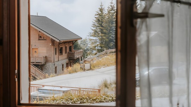 Une fenêtre donnant sur un immeuble, une porte en bois et un rideau orné d’un motif représentant des arbres.