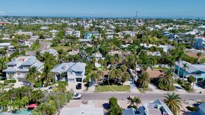 An aerial view of a coastal residential area with houses, palm trees, and a clear view of the ocean.